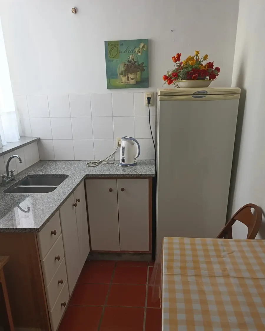 La cocina para huéspedes, con heladera, pava eléctrica y una mesa con mantel a cuadros.
