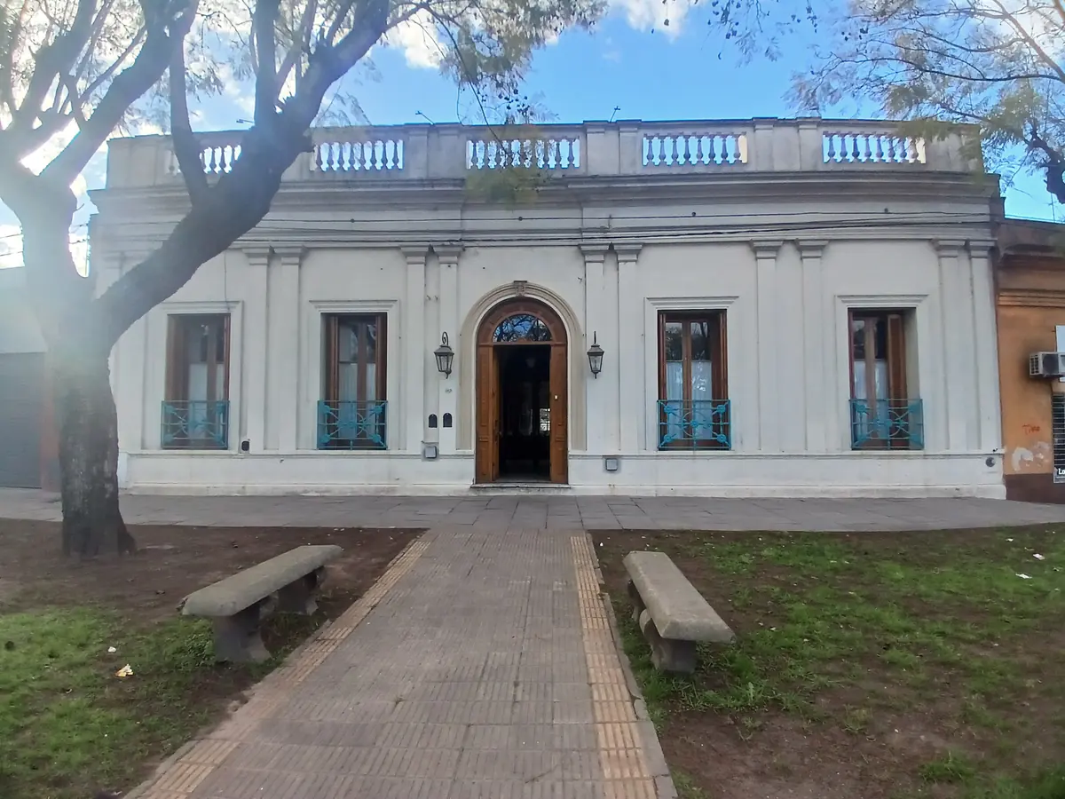 La fachada del hotel de frente, con el camino de entrada y los bancos de la vereda.