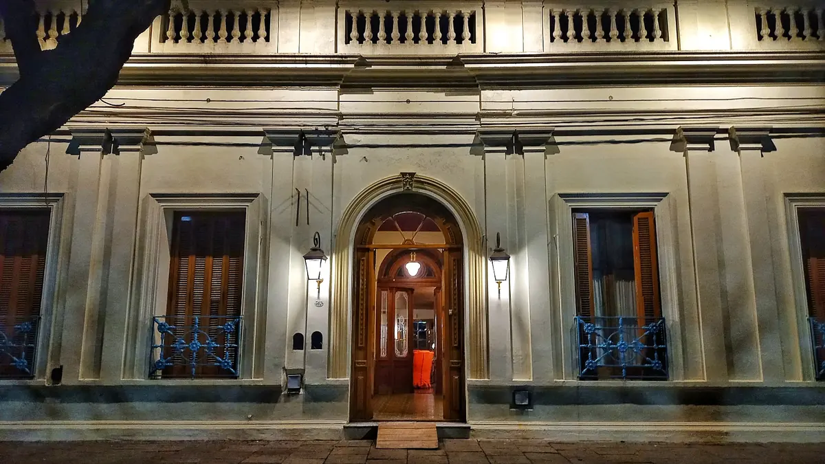 La fachada del Hotel Chascomús de noche, con la puerta en arco iluminada y los balcones de reja.