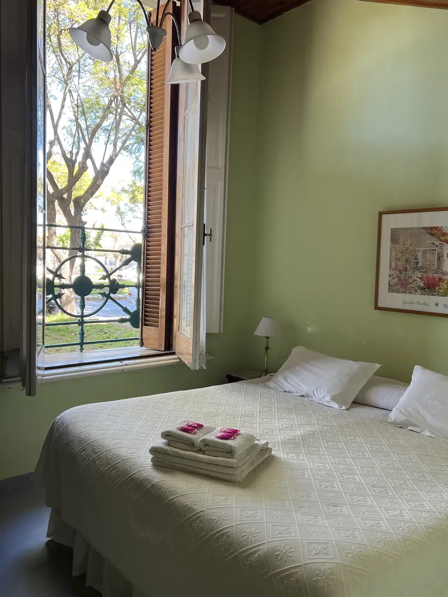 Habitación doble con paredes verdes y una ventana alta con reja.