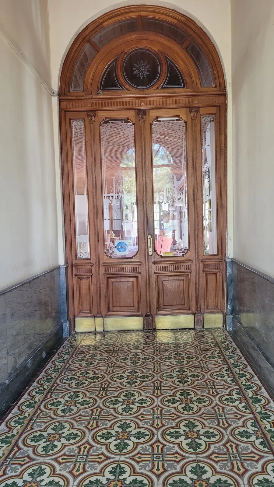 La puerta tallada al final del zaguán, sobre el piso de baldosas.